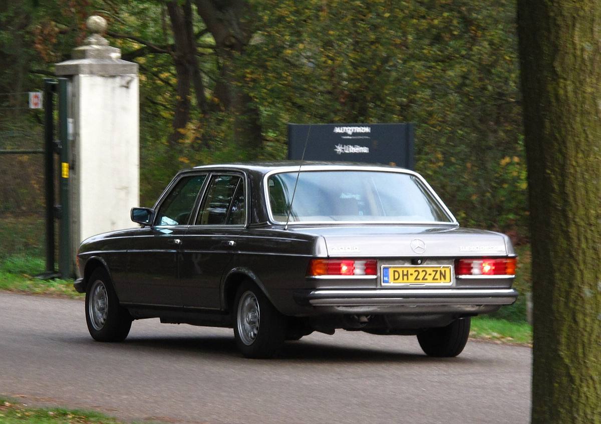 Záď tmavého sedanu Mercedes řady 123 s rozsvícenými koncovými svítilnami