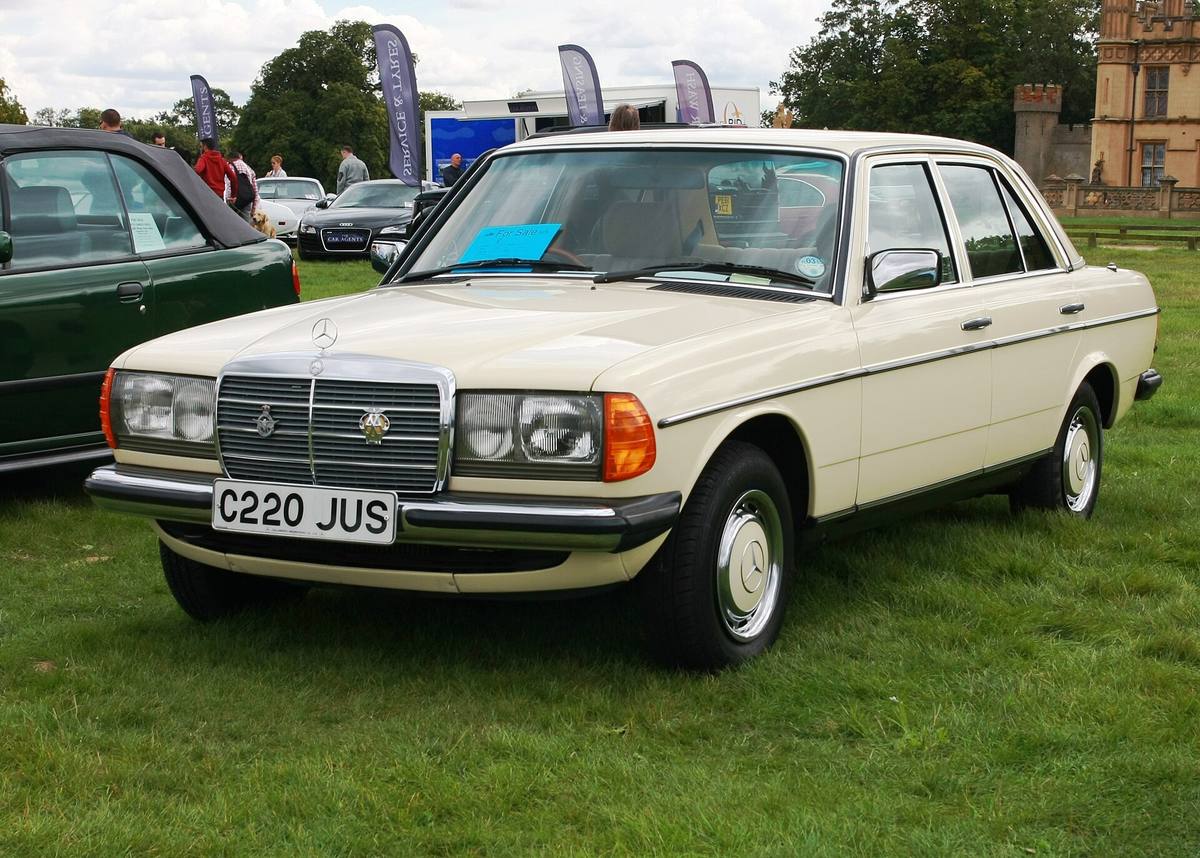 Béžový sedan Mercedes-Benz 230 E řady 123 s britskou registrační značkou na výstavní louce
