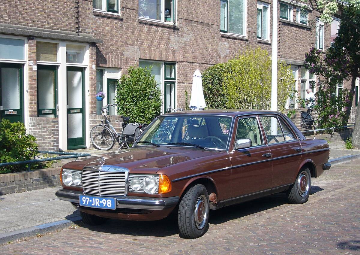 Hnědý sedan Mercedes-Benz 230 řady 123 z roku 1976 zaparkovaný před cihlovými řadovými domy