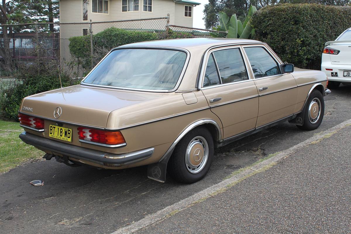 Béžový sedan Mercedes-Benz 280 E řady 123 zezadu z boku, zaparkovaný u chodníku