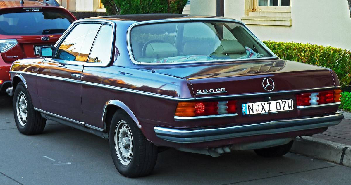 Tmavě červené kupé Mercedes-Benz 280 CE řady 123 z roku 1985 zezadu, zadním oknem jsou vidět světlé potahy sedadel
