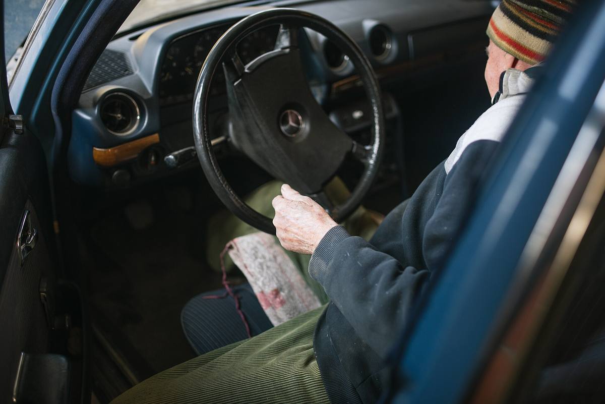 Řidič za volantem naftového Mercedesu-Benz 200 D řady 123 s modrou přístrojovou deskou